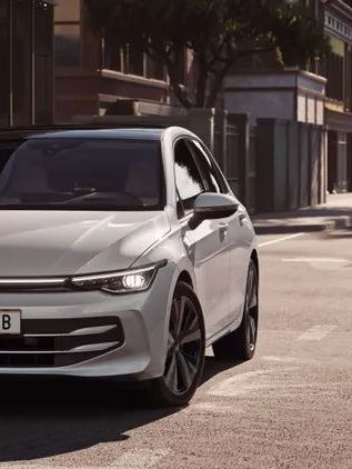 VW Golf Weißer VW Golf fährt auf einer Straße auf eine Kreuzung zu.