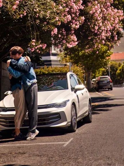 VW Golf Weißer VW Golf wird an einer Ladestation geladen. Zwei Männer haben sich neben dem Auto in den Armen.